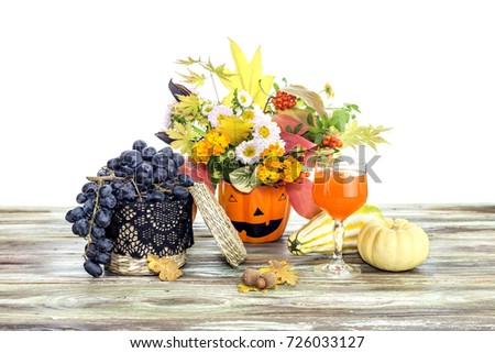 Decoration of a table for Halloween. Grapes, glass with juice, autumn leaves and flowers in a vase on a wooden table close-up on a white background.