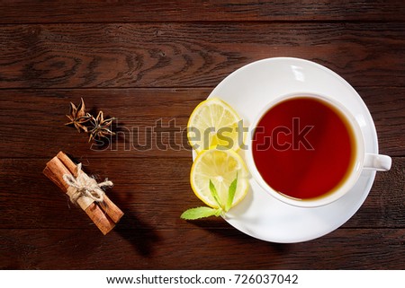 White cup of tea with cinnamon sticks, lemon, mint leaves and tea strainer on wooden rustic table.