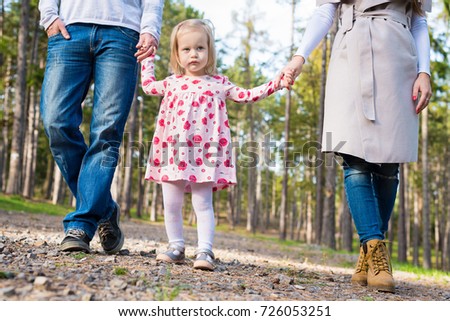 Happy young family taking a walk in a park, family holding hands walking together along forrest path