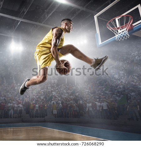 Basketball player on big professional arena during the game. Basketball player makes slam dunk. Player wears unbranded clothes.