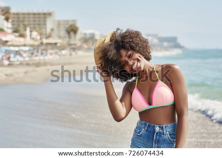 Afro american woman holding hat on head laughing at seaside