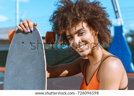 young african-american woman in bright sports bra posing with longboard