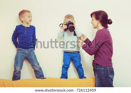 Child passion and hobbies concept. Kid playing with big professional digital camera, photographing various things in house, mother looking after him.