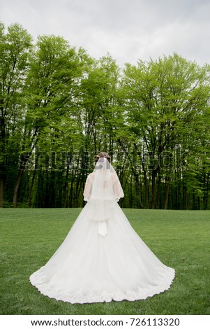 The bride is standing with her back on the grass