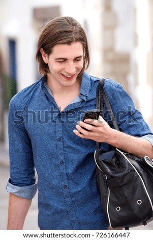 Portrait of handsome man with long hair holding smart phone and bag