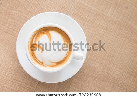 A cup of coffee with Latte pattern in a white cup on wooden background. Free space.