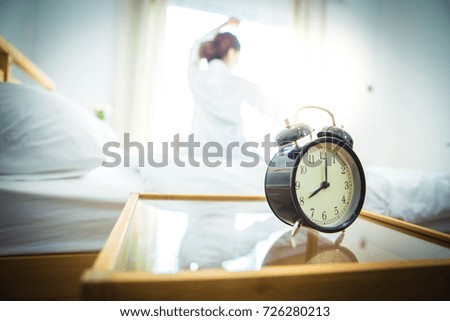 A black alarm clock is displayed at eight o'clock in the morning ,Woman stretching in bed after waking up.