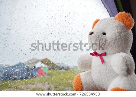 A white teddy bear is placed next to the mirror in the car with rain falling. The concept of expressing emotions and feelings. Selective focus.

