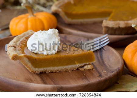 Slice of pumpkin pie and whipped cream topping with pumpkin and sliced whole pie in background