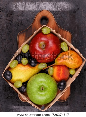 Red apple, dark blue grapes, green apple, yellow pear, green grapes, orange peach in a wooden box on a metallic background in retro style
