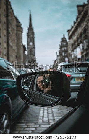 Young woman photographer taking pictures with camera reflected in the rear view mirror of a car on the streets of Edinburgh.