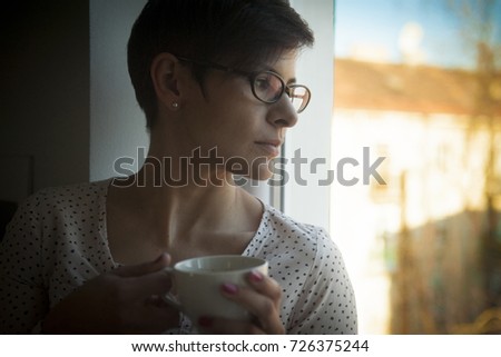 young short haired woman drinking coffee and looking out the window