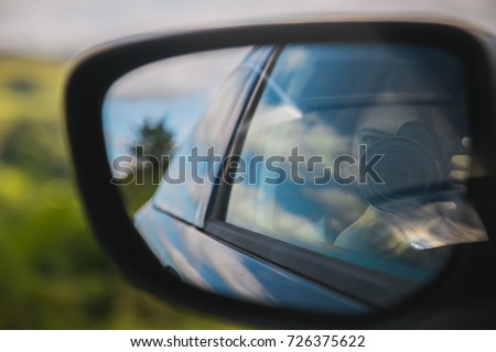 Young woman taking pictures with camera reflected in the rear view mirror of a car. Low contrast filter. 