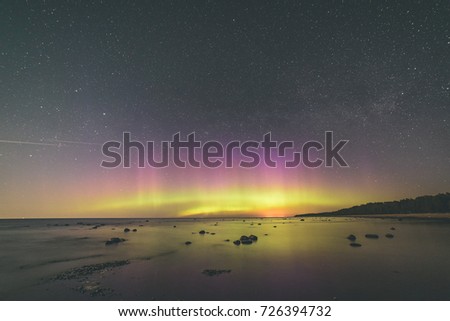 Intense northern lights (Aurora borealis) over Baltic sea. rocky beach - vintage film look