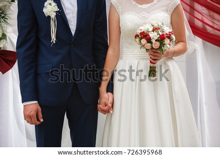
wedding ceremony.
Newlyweds are hold hands .
young men and women hold each other hands.
newlyweds during the marriage ceremony.
the bride holds a bright bouquet with red flowers