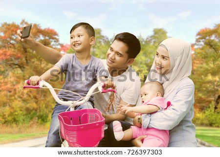 Muslim family playing with their children while using a smartphone to take a picture together in the park. Shot at autumn time