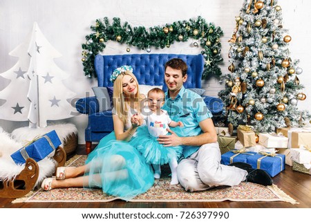 Modern Christmas Family Portrait sitting and smiling In Home Holiday Living Room, Mother, father and Kid Baby waiting Santa With Present Gift Box, House Decorating By white Xmas Tree Candles Garland