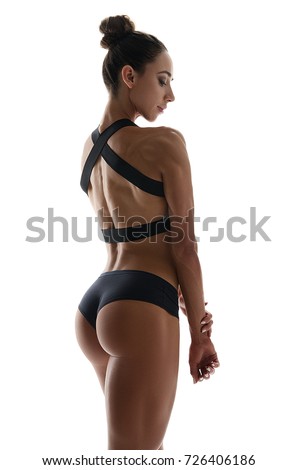 Muscular young woman athlete in sports clothing standing turning back looking down on white background. Woman bodybuilder relaxing after exercise. 