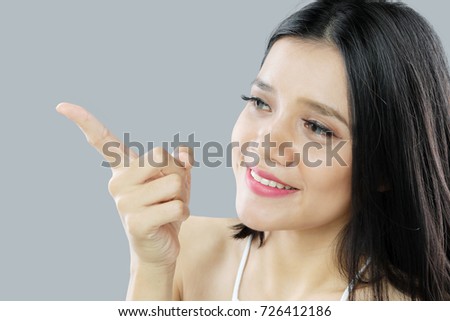 Picture of beautiful woman pointing something with her finger. Shot at grey background