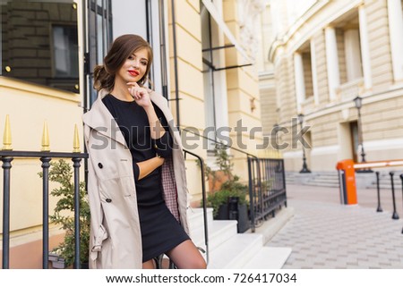 stylish pretty woman is posing at camera and smiles on the street. Charming girl with red lips and big green eyes. Real emotions of charming woman. Outdoor portrait of attractive woman.