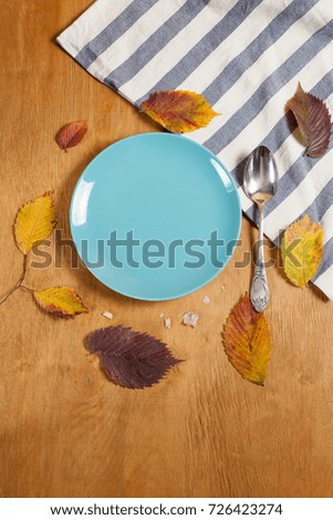 an empty blue plate on a wooden background surrounded by autumn leaves. with a place for your inscription