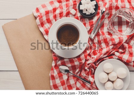 Morning coffee at restaurant. White porcelain cup of black bitter coffee with treats on stylish checkered tablecloth and craft paper on wooden background, top view, copy space