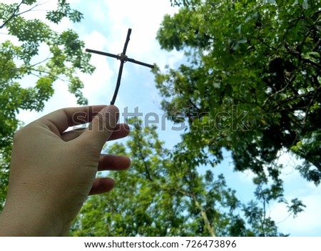 Close up hand holding wooden strength Christ cross with blurry natural tree and sky background