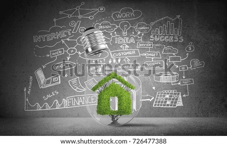 Lightbulb with green house sign inside placed against sketched business plan information on grey wall. 3D rendering.