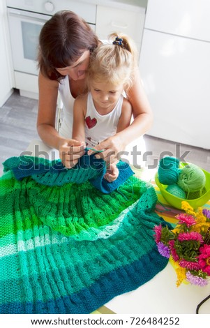 Mom teaches my daughter to knit a green knitted fabric of thick 