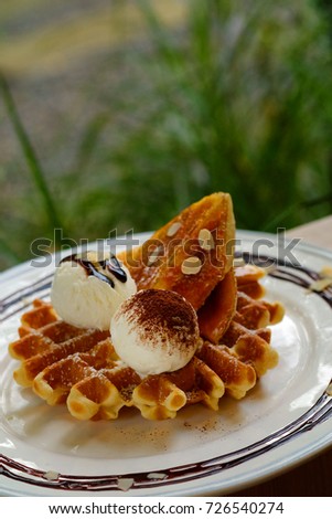 tasty waffle and vanilla ice cream set served with banana sugar coating Topped with chocolate sauce on white plate in green garden coffee shop mood tone. Have some space for write wording