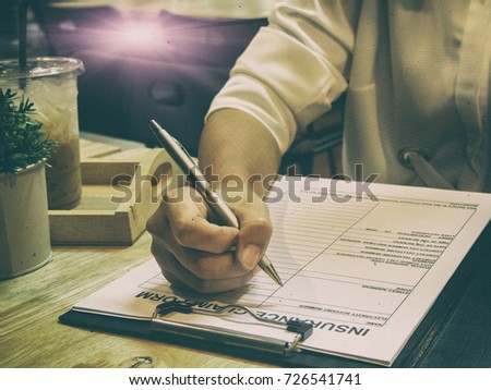 The classic old film design background of the human hand with pen is signing on The Insurance Claim Form,Fill the information form on wooden desk,vintage tone.grainy film design
