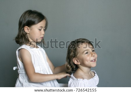 The girl makes the hair of her younger sister