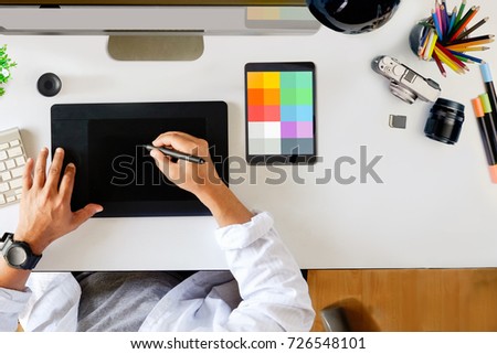Designer drawing on digital tablet at workspace top view with essential elements on white table.