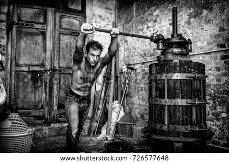 Shirtless winemaker farmer working on a old wine press. Black and white picture