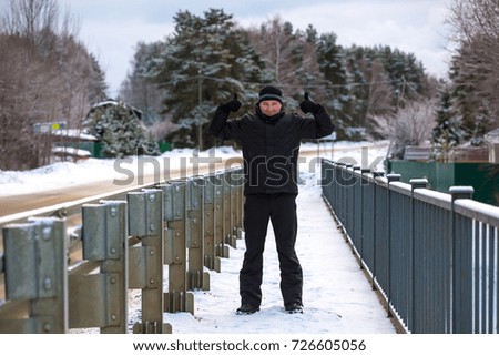 A cheerful man in black winter clothes is holding two fingers up and welcomes you to Russia