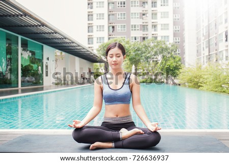 Young asian woman doing yoga moves or meditating by the pool, Asian girl start her yoga class with meditation. Sport recreation holiday concept