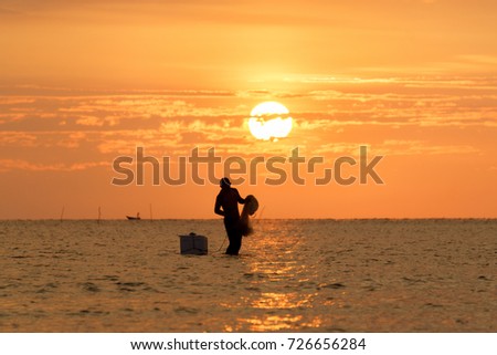 People in silhouette casting a fishing net with orange sunset color at background.Good image for adventure, struggle and success story photo.