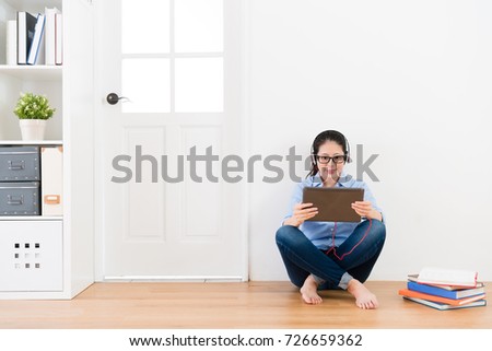 smiling beauty woman student finished school homework sitting on wooden floor with white wall background relaxing and using mobile digital tablet watching online video.