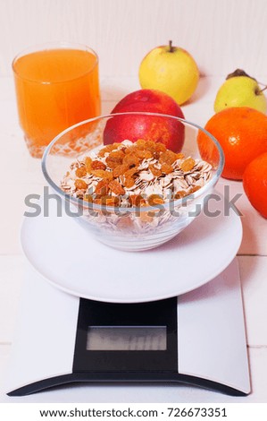 digital kitchen scales on light wooden table with oatmeal raisins, juice, tangerines, apples and peach. concept of healthy eating