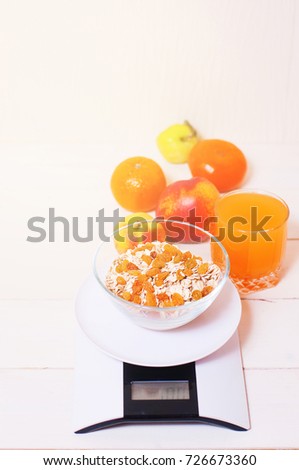 digital kitchen scales on light wooden table with oatmeal raisins, juice, tangerines, apples and peach. concept of healthy eating