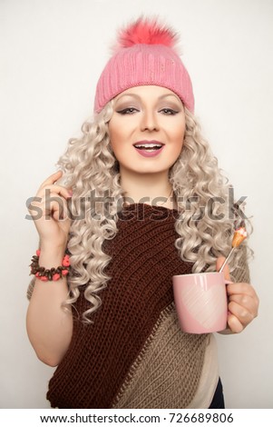 pretty young woman wearing pink knitted hat standing with cup of tea and touching her hair on white background isolated