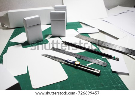 Product cosmetic packaging template boxes structure design and development workshop on cutting board with tools. Handcraft design with equipment such as cutter knife, ruler, pencil.