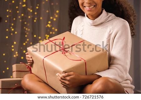 Cropped picture of a smiling young woman sitting on a floor in her room with present