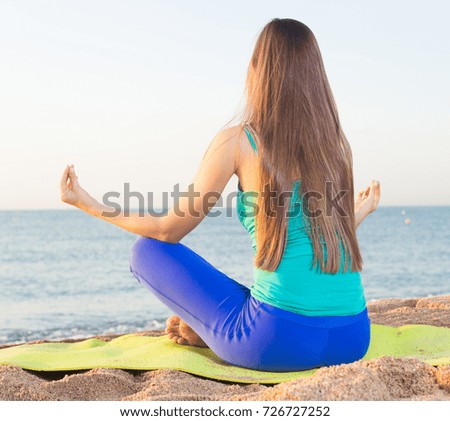 Young woman in blue T-shirt is sitting and practicing asana on nature.