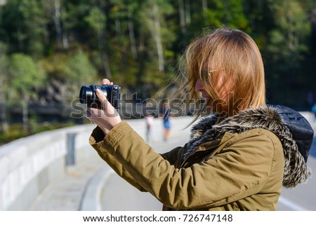 Female, model taking a picture with her camera at the lake Vidraru