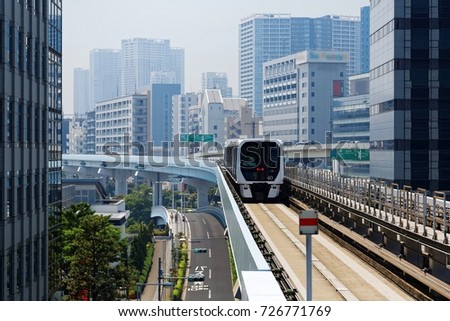 Scenic view of a train traveling on elevated rails of Yurikamome Line in Downtown Tokyo, with a background of modern buildings near Takeshiba Station under blue sunny sky ~ Scenery of a vibrant city