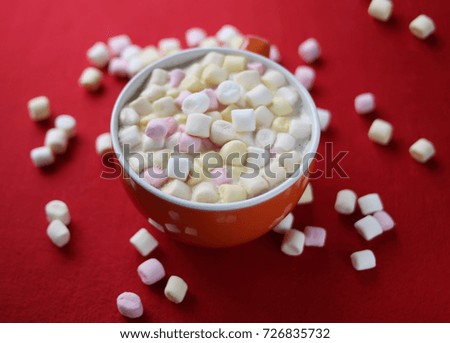 Cocoa drink with marshmallows in orange cup on red background.