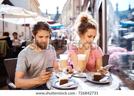 Young couple with smartphones sitting in cafe.