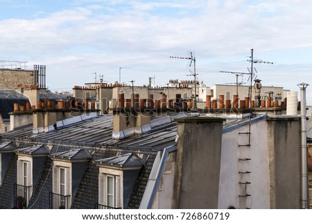 View on roofs of Paris with chimneys and antennas against blue sky.