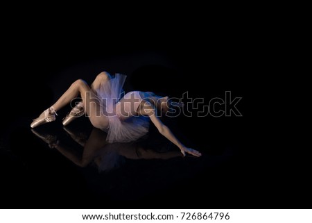 Girl ballerina posing and performing dance elements in blue scenic light on a black background